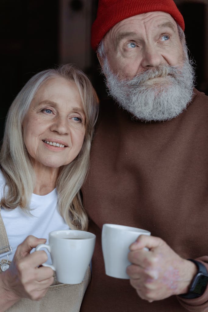Joyful senior couple sharing a warm moment with coffee cups indoors.