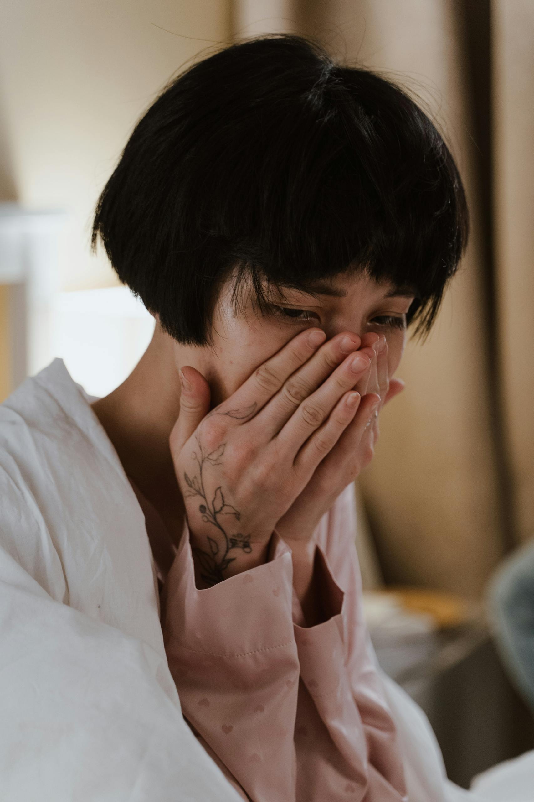 Portrait of a woman expressing sadness, hands covering face indoors.